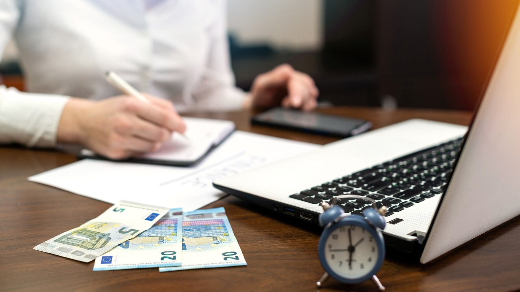 femme-travaillant-finances-table-ordinateur-portable-smartphone-argent-bloc-notes-horloge